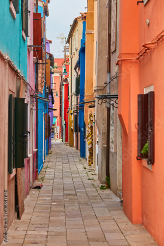 Burano island narrow cobblestone street between colorful houses buildings with multicolored bright walls, blue sky sunny summer day, Venice Province, Veneto Region, Northern Italy.