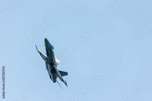 A super hornet F-18 jet fighter in an Air show festival ascending at subsonic speed in a clear blue sky with condensation wakes in its wings