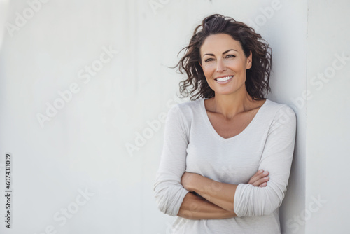 Smiling middle age woman standing in front of a white wall. Generative AI.