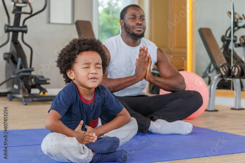 Cute boy in sportswear with her smiling black african american dad meditating on a yoga mat