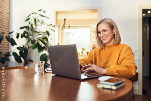 Happy mature woman using laptop while working remotely from home in living room