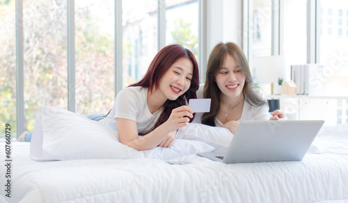 Asian young cheerful female LGBTQ lover couple partner traveler lay down on bed using laptop notebook computer reserve hotel and transportation via internet online on bed