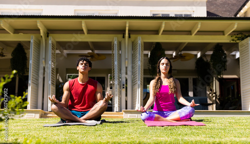 Biracial young couple practicing meditation while sitting on mats in yard against house