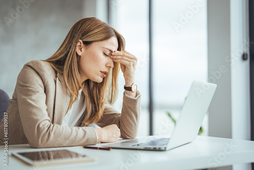 Exhausted businesswoman having a headache in modern office. Mature creative woman working at office desk with spectacles on head feeling tired. Stressed casual business woman feeling eye pain 