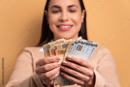 hands of brunette young woman showing money, brazilian currency in beige background. business, loan, pay, wealth concept. 