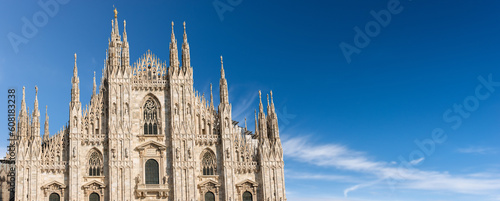 Facade of the Duomo di Milano against a clear blue sky with clouds and copy space. (Milan Cathedral 1418-1577). Church, monument symbol of Lombardy, Italy, Europe. 