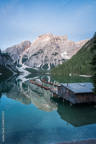 Grüner See in den Bergen mit Booten und einer Holzhütte mit glattem Wasser und Spiegelung zur blauen Stunde vor Sonnenaufgang.