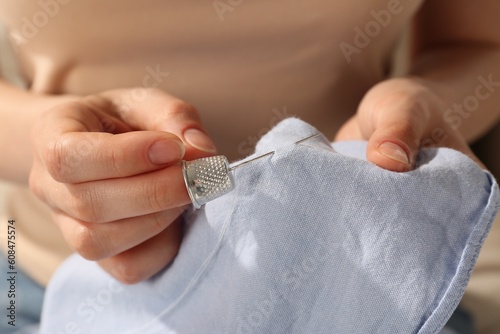 Woman sewing on light blue fabric with thimble and needle, closeup