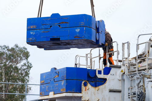 Worker in hi-vis and hard hat guides heavy steel counterweight into place on 1000 ton mobile crane