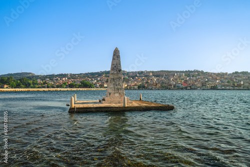 1813 stone-built water-surrounded obelisk next to De Bosset Bridge with Argostoli town panorama in the background on the Ionian Island of Cephalonia Greece.