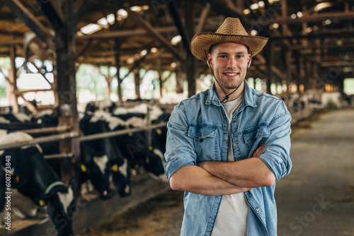 Portrait of a happy farmer standing in a barn full of cows.