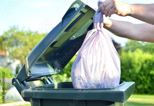 Person throws a plastic bag of garbage into a street green trash can.