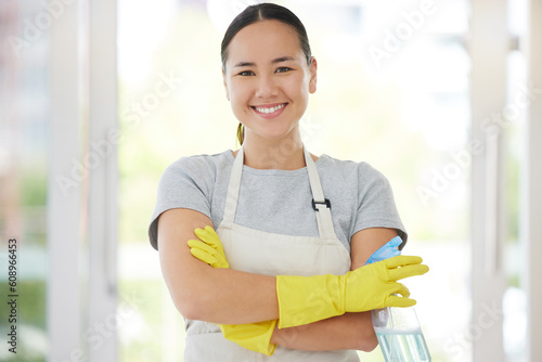 Portrait, cleaning and arms crossed with a woman housekeeper using disinfectant to remove bacteria in a home. Safety, smile and hygiene with a confident young female cleaner working in a living room