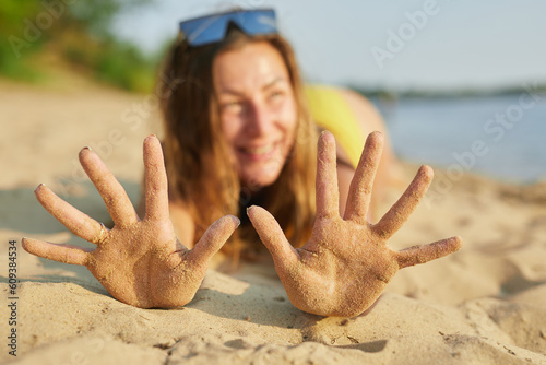 Happy girl with hands in the sand on the beach.Hands with grains of sand. The concept of summer holidays.