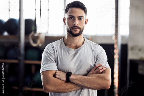Fitness, exercise and portrait of a serious man at gym for a training workout with focus. Face of male athlete or personal trainer with strong muscle, power and motivation with arms crossed at club