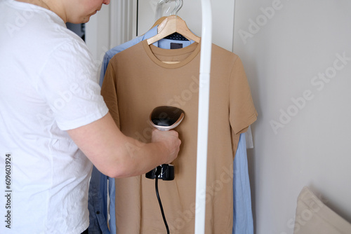 A young man holds the garment steamer in his hand and smoothes the t-shirt after washing and drying