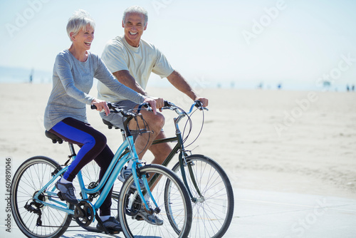Senior couple riding bicycles on beach boardwalk