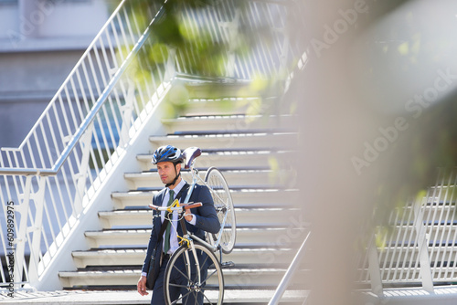 Businessman in suit and helmet carrying bicycle down urban stairs