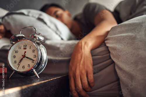 Alarm clock, relax and man sleeping in the bed of his modern apartment in the morning. Lazy, resting and closeup of a timer bell with a male person taking a nap and dreaming in bedroom at his home.