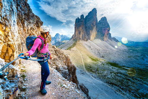 Young athletic woman enjoys scenic view on Tre Cime from via ferrata in the evening. Tre Cime, Dolomites, South Tirol, Italy, Europe.
