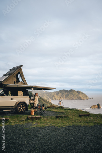 A Camping car with rooftop tent on a cliff with a view of sea and island with a couple during the sunset with blue sky and clouds in Izu Peninsula, Japan.