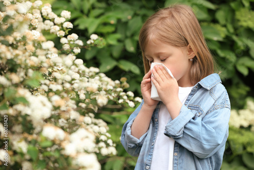 Little girl suffering from seasonal pollen allergy near blossoming tree on spring day