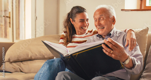 Portrait of a Nostalgic Woman Bringing the Family Photo Album to her Senior Father so They Can Watch Photos Together. Old Man Sharing Funny Memories and Stories with his Daughter 