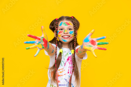 A little girl with bright colors painted, a little girl is fond of drawing, A child with paints on a yellow isolated background. Children's leisure, a schoolgirl at a drawing course.
