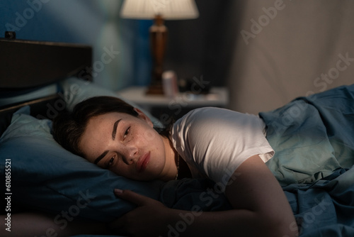 Young sad woman lying in bed late at night trying to sleep suffering insomnia. Girl in bed scared on nightmares looking worried and stressed. Sleeping disorder and insomnia