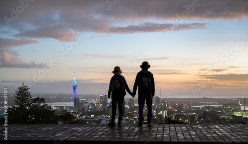 Silhouette image of couple standing on Mt Eden summit and watching sunrise over Auckland city. Selective focus on people in foreground.