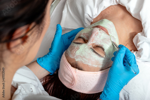 The beautician applies a collagen booster on the client's face. Middle aged woman receiving spa treatment in a beauty salon.