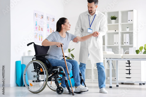 Male physiotherapist helping young woman to stand up in rehabilitation center