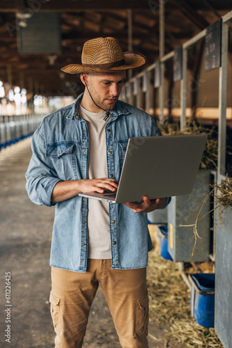 Front view of a man with a laptop standing in a big animal farm.