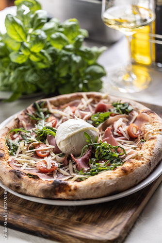 Round buffalo mozzarella on top of a ham, tmatoes and rocket pizza with crusty edges