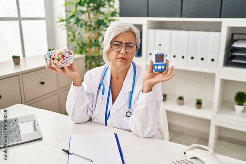 Middle age woman with grey hair wearing doctor uniform holding glucose monitor depressed and worry for distress, crying angry and afraid. sad expression.