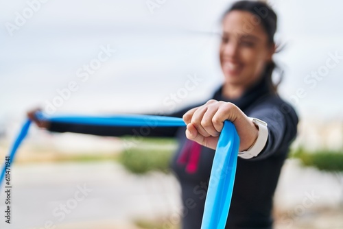 Young hispanic woman wearing sportswear training using elastic band at street