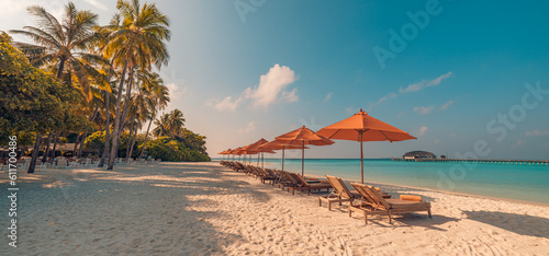 Fantastic panoramic view. Sandy shore soft sunrise sunlight over chairs umbrella and palm trees. Tropical island beach landscape exotic coast. Summer vacation, holiday. Relaxing sunrise leisure resort