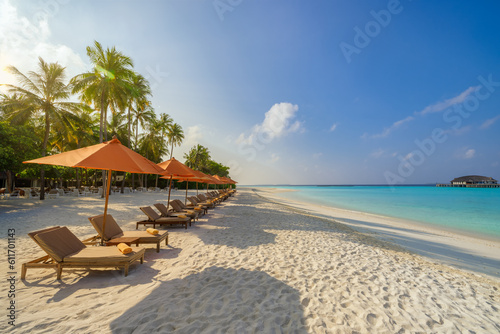 Fantastic panoramic view. Sandy shore soft sunrise sunlight over chairs umbrella and palm trees. Tropical island beach landscape exotic coast. Summer vacation, holiday. Relaxing sunrise leisure resort