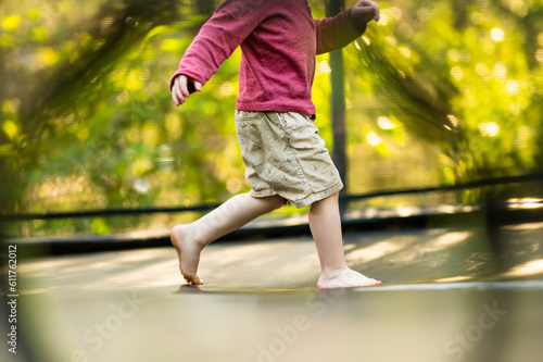 Cute toddler boy jumping on a trampoline in a backyard on warm and sunny summer day. Sports and exercises for children.