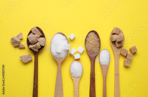 Spoons with different types of sugar on yellow background, flat lay