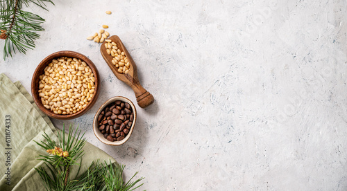 Pine nuts in a bowl and wooden scoop on a napkin on a light texture background with branches of pine needles. The concept of a natural, organic and healthy superfood and snack.