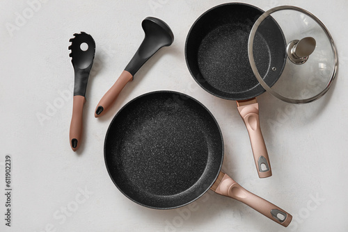 Frying pans and kitchen utensils on light background