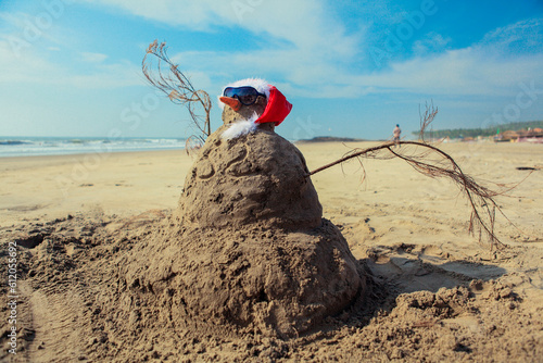 Funny Snowman in Sunglasses and Santa Red Hat, made of the Sand on Goa beach, India