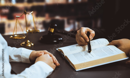 Closeup lawyer colleagues preparing for lawsuit or litigation, reading and pointing hand on legal book on desk at library for educational law school concept, decorated with legal symbols. Equilibrium