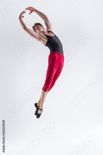 Contemporary Ballet of Young Flexible Athletic Man Posing in Red Tights in Flying Dance Pose With Hands Connected in Studio on White.