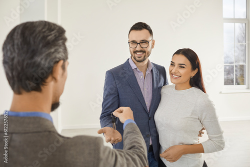 Young family couple buying a new modern house or flat. Real estate agent or realtor gives the house key to a happy young man and woman. Real estate, property purchase, mortgage concept