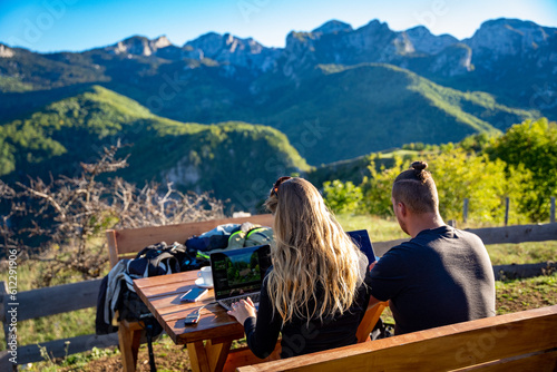 Young couple working remote as digital nomads in the sunshine on a mountain in Montenegro with a great view