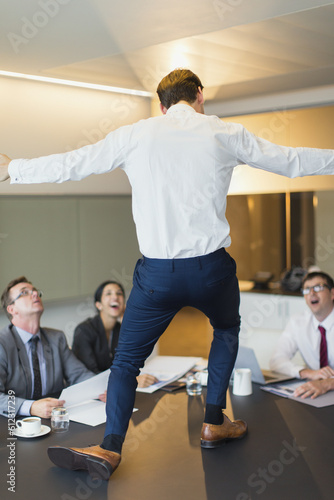Surprised colleagues watching exuberant businessman dancing on conference table