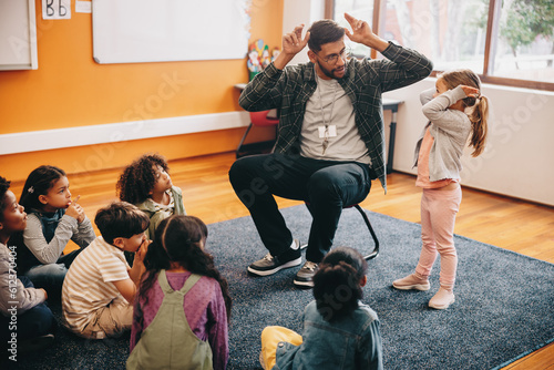 Male educator in a primary school class. Teacher shows a little girl how to do heads and shoulders