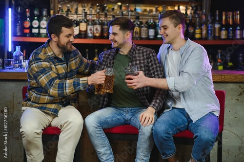 Sport, people, leisure, friendship, entertainment concept - happy male football fans or good yuong friends drinking beer, celebrating victory at bar or pub. Human positive emotions concept